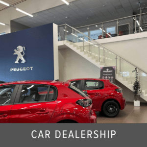 Indoor glass stair balustrade with stainless steel handrail inside a Peugeot car dealership, featuring red vehicles and mezzanine level.