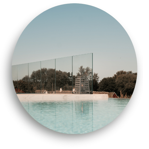 Frameless glass balustrade installed by a pool, creating a wind-protected area with unobstructed views. Clear safety glass offers a discreet and exclusive frame for the poolside.