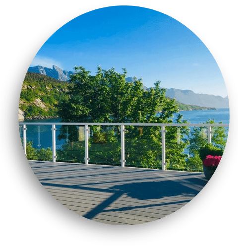 Aluminium glass balustrade on a sunlit terrace overlooking a lake, surrounded by mountains and greenery.