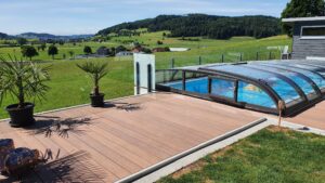 Defined pool area with modern glass balustrade, retractable pool cover and timber decking in a rural setting with rolling green hills.