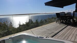 Modern frameless glass balustrade on coastal deck with timber flooring and shaded seating beneath an awning.