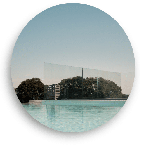 Clear, post-free glass balustrade installed by a pool, with large glass panels secured in a discreet bottom profile. The view remains uninterrupted, with soft reflections from the sky creating a serene setting.