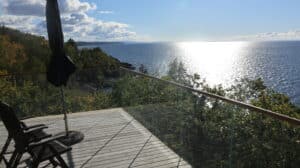 Corner-mounted clear glass balustrade with wooden handrail, offering sweeping views of ocean and forest landscape.