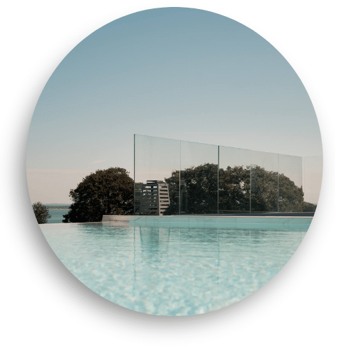 Post-free glass balustrade by a poolside edge with wide open views of treetops and the distant sea.