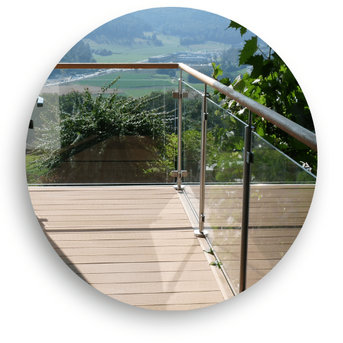Glass balustrade with timber handrail on a wooden deck, overlooking a forested valley and rugged hillside landscape.