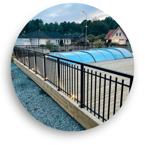 Black powder-coated aluminium railing in wrought iron style, forming a boundary around the timber decking and pool enclosure.
