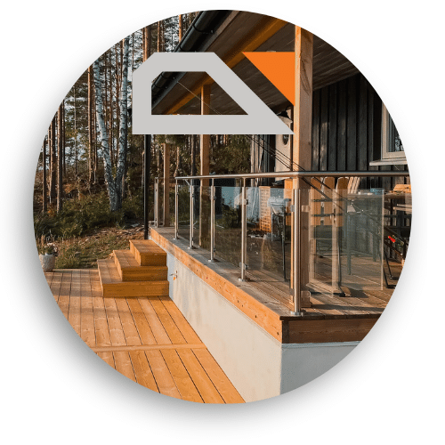 A deck with glass balustrade and stainless steel posts surrounds a timber cabin in a forest setting. The railing offers open views while framing the outdoor space with safety and elegance.