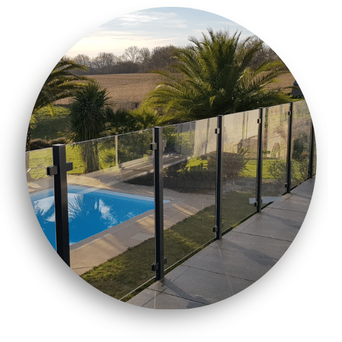 Pool fence with black powder-coated posts and clear laminated glass panels, set within a lush garden environment.