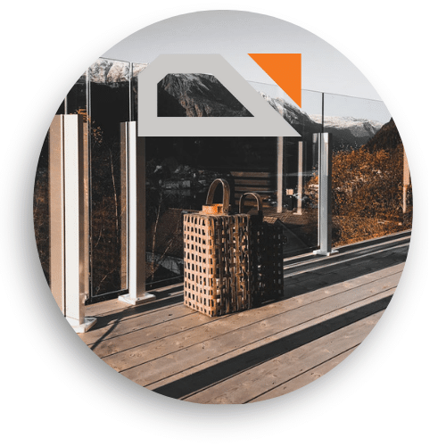 Glass balustrade with white posts and clamps mounted on a wooden deck. The transparent glass panels frame a scenic view of mountains and valley. Two decorative lanterns sit on the decking.
