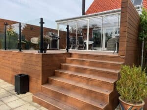 High-level deck with black aluminium and clear glass balustrade, brown timber decking and multi-level stair access.