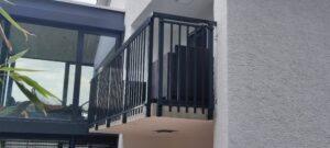 Sleek black metal Juliet balcony installed on rendered façade of a modern home with glazed double doors.