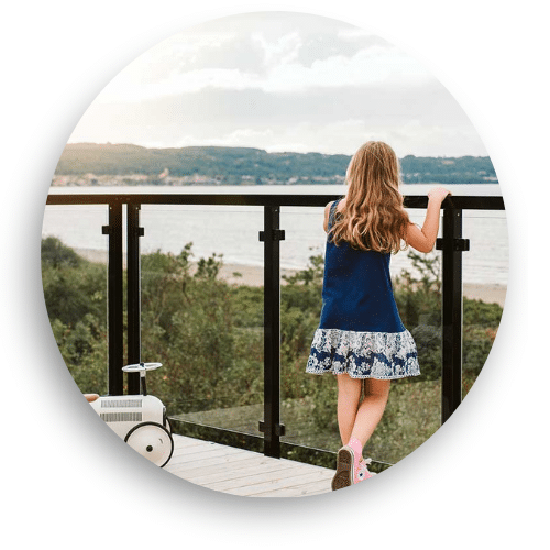 Black aluminium and clear glass balcony railing with lake view, with a young girl standing safely by the rail.