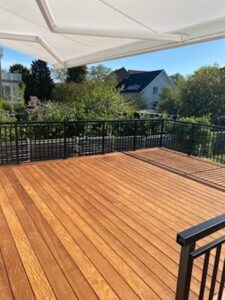 Traditional black wrought iron railing around wooden terrace with sun canopy, leafy backdrop and natural light.
