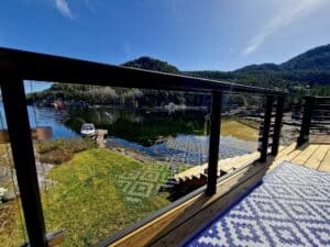 Black post glass balustrade on deck by the water, facing jetty, boat and green mountain landscape.