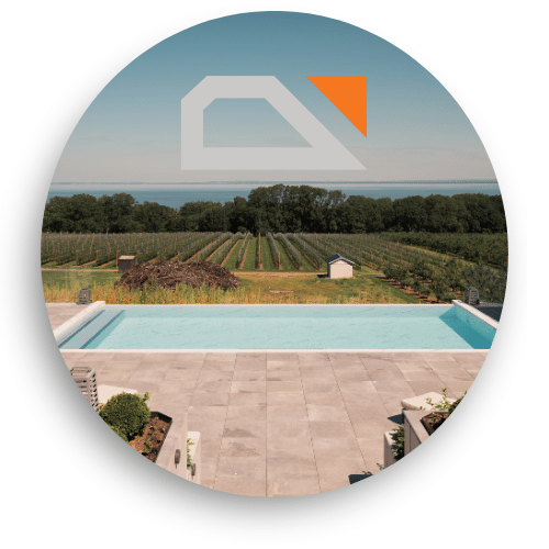 Glass railing with uninterrupted views over fields and sea, seen from a modern terrace beside an infinity pool.