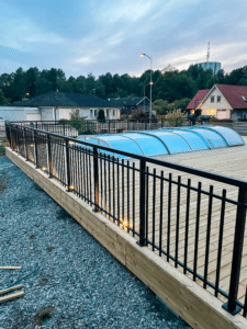 Powder-coated black aluminium railing in Alu Retro design enclosing timber-decked pool area, combining classic aesthetics with high safety.
