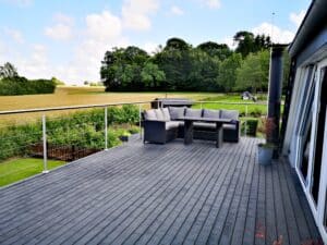 Stainless steel wire railing on grey deck, outdoor lounge seating with uninterrupted views of open fields and farmland.