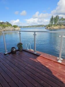 White post and clear glass railing on waterside terrace, with flower pots and ladder leading to the sea.