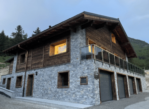 Balcony with smoked glass and stainless steel posts on stone house with timber cladding in mountain surroundings.