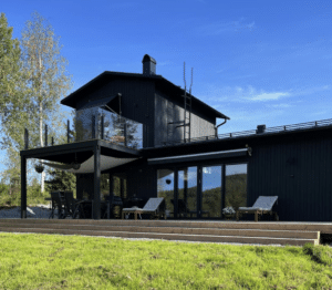 Upper wooden deck with black post and smoked glass balustrade, installed on modern house with dark timber façade.