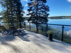 Sleek black aluminium and clear glass railing on deck by lake, with tree backdrop and open natural surroundings.