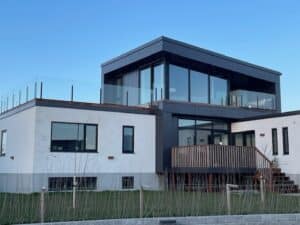 Minimalist frameless glass balustrade around rooftop deck of modern home with white and black exterior architecture.