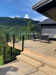 Deck with sleek black aluminium frameless glass railing, offering views of trees, hills and open blue sky.