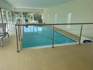 Sleek indoor pool railing with stainless steel posts and horizontal wire, placed beside glass walls for a refined safety barrier.