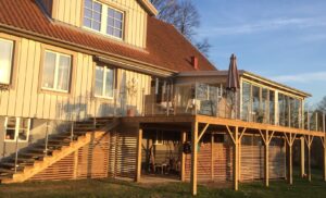 Clear glass and stainless steel railing along timber stairs and multi-level deck, attached to sunlit garden room façade.