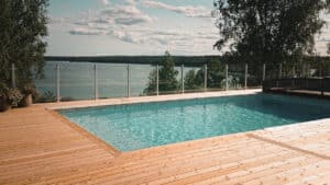 Glass fence around garden pool with timber decking and lake view – combines natural beauty with reliable safety and transparency.