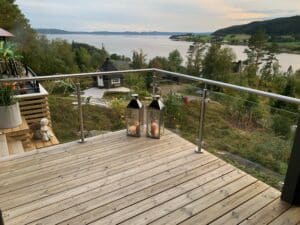 Timber deck with clear glass and stainless steel railing, facing lake, greenery and decorative garden elements.
