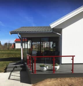 Glass screen with red aluminium posts and clear panels on grey terrace. Two white planters and a sunroom in the background.