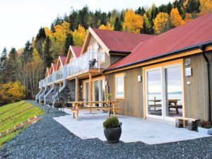 Stylish row of cabins with balconies fitted with white post glass screens. Autumn foliage, stone terrace and outdoor seating.