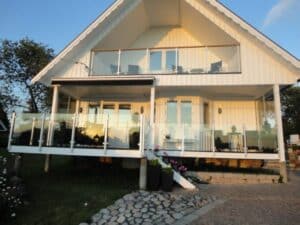White timber house with stainless steel post glass railings on both balcony and terrace, reflecting warm evening sunlight.