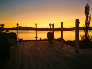 Lakeside terrace with glass privacy screen and white posts, bathed in golden sunset light reflecting in still water.