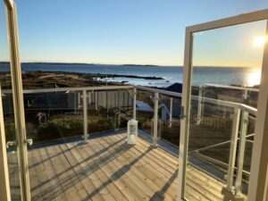 Glass privacy screen with white aluminium frame on balcony with open doors, overlooking sunset across sea and islands.