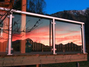 White aluminium framed glass screen on terrace, reflecting vibrant sunset over distant hills and colourful skies.
